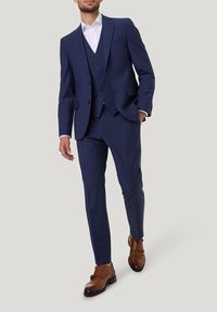 Marineblaues dreiteiliges Anzugset mit taillierter Passform, bestehend aus einem einreihigen Blazer, einer Weste und schmal geschnittenen Hosen. Braune Lederschuhe.