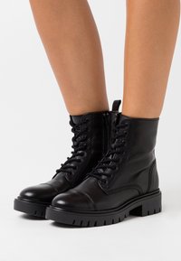 Svarta läderankelstövlar med rund tå, snörning fram, sidodragkedja och texturerade gummisulor. Utrustade med vadderade kragar och minimal sömnad.