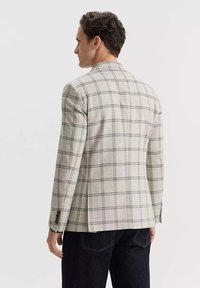 Jasnoszara marynarka w kratę z brązowymi i granatowymi akcentami, z wyraźnymi ramionami i pojedynczym wentylacyjnym otworem z tyłu, wykonana z teksturowanej tkaniny.