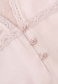 Tissu rose doux avec trois boutons assortis et une délicate bordure en dentelle le long du bord, suggérant un gros plan sur un détail de vêtement.