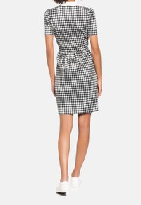 Mustat ja valkoiset ruututapetit, joissa on lyhyet hihat, istuva vartalo, ker gathered vyötärö ja suora helma, yhdistettynä valkoisiin tenniskenkiin.