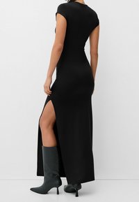 Svart figursydd klänning med korta ärmar och en sidoklyvning, tillverkad av slätt material. Kombineras med knähöga svarta klackstövlar.