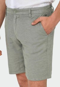 Shorts gris clair en tissu texturé avec une coupe régulière. Les caractéristiques comprennent une fermeture à bouton, des poches latérales et des détails de couture discrets.