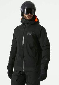 Zwarte waterdichte skijas met een oranje gevoerd capuchon, full zip sluiting en bijpassende handschoenen. Voorzien van een logo op de borst en verstelbare manchetten.