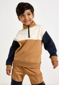 Hanorac color-block în nuanțe de bej, crem și bleumarin. Are guler în picioare, fermoar până la mijloc și manșete reiate. Textură moale. Asortat cu pantaloni în aceeași nuanță.