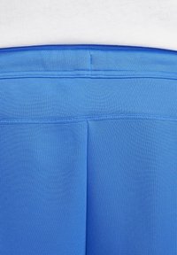 Nära bild av bakseam och midjeresår på blåa träningsleggings som bärs med vit topp.