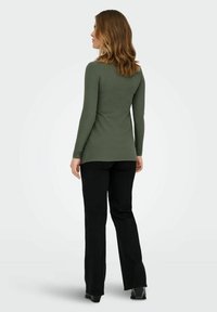 Olivgrünes, geripptes Langarmtop mit rundem Ausschnitt, kombiniert mit schwarzen, weit geschnittenen Hosen. Die Textur wirkt enganliegend mit einem dezenten Muster.
