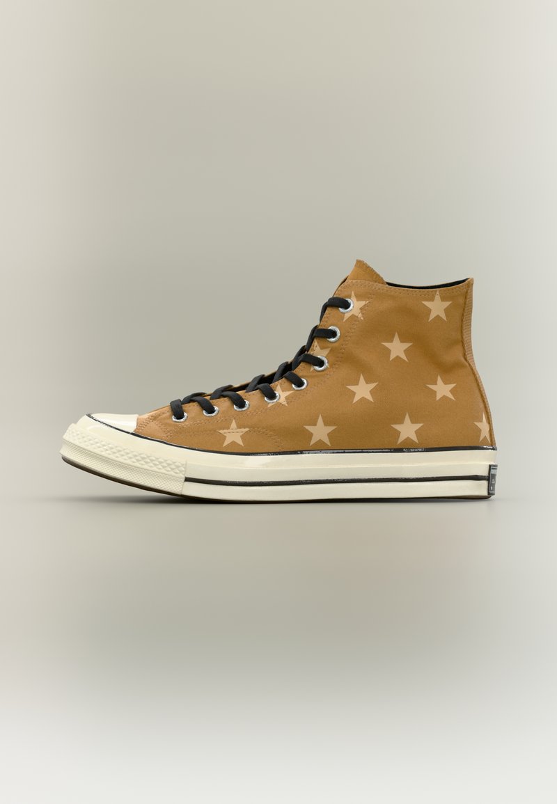 Kõrge säärega pruun lõuendist toss tume tähtede mustriga, mustad paelad, valge kummist talla ja musta triibuga detailiga neutraalsel taustal.