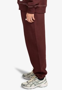 Bordeaux joggings met een elastische tailleband en boorden, gecombineerd met grijs-witte sportschoenen met mesh panelen en veters.