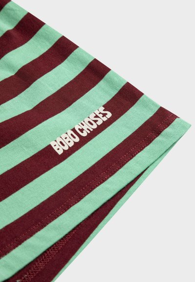 Gros plan sur un tissu à rayures vertes et rouge foncé avec le texte blanc "BOBO CHOSES" imprimé près de l'ourlet.