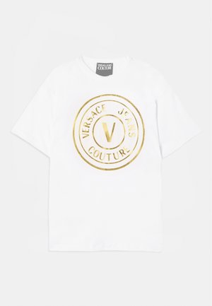Hvit bomulls t-skjorte med et stort gull sirkulært logo som har "VERSACE JEANS COUTURE" og et sentralt "V"-design. Korte ermer, rund hals.
