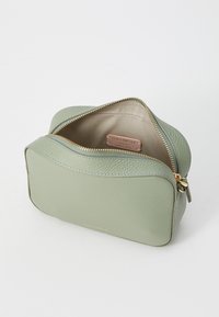 Green leather cosmetic bag with zip closure and gold hardware. Contains a beige interior with a brand label. Rounded design and textured surface.
