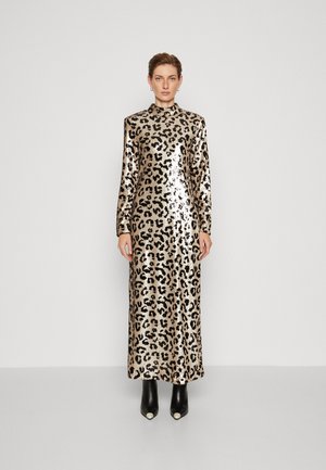 Maxi mekko leopardikuvioinnilla, jossa on pitkät hihat, korkea kaula-aukko ja kiiltävä paljettil fabric. Malli käyttää mustia nilkkureita, joissa on valkoisia yksityiskohtia.
