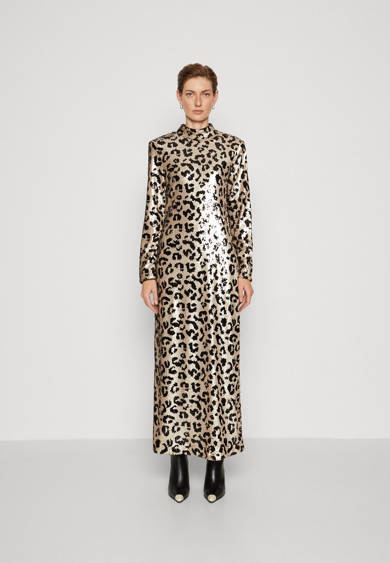 Maxi mekko leopardikuvioinnilla, jossa on pitkät hihat, korkea kaula-aukko ja kiiltävä paljettil fabric. Malli käyttää mustia nilkkureita, joissa on valkoisia yksityiskohtia.
