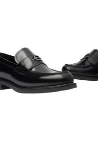 Mocassini neri in pelle con una fascia rialzata, hardware di accentuazione in argento, punta arrotondata e suola nera strutturata. Cuciture dettagliate lungo i bordi.