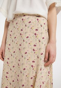 Gonna midi con stampa floreale in beige chiaro, con fiori viola e verdi e steli delicati. Tessuto liscio con un design fluido.