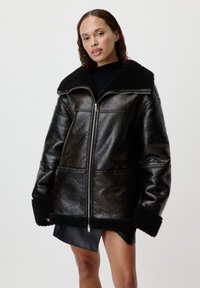 Giubbotto in pelle nera con colletto e polsini in shearling, dotato di zip frontale e vestibilità comoda, che mette in risalto una texture liscia e una superficie lucida.