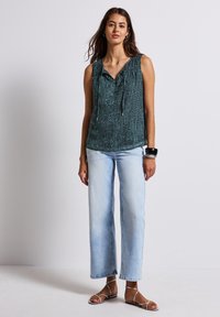 Teal sleeveless blouse with a textured design and drawstring neckline, paired with light blue wide-leg jeans and flat sandals.