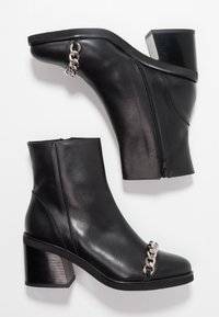 Bottes basses en cuir noir avec un talon épais, ornées d'une chaîne argentée et d'une fermeture éclair latérale, texture lisse et bout rond.