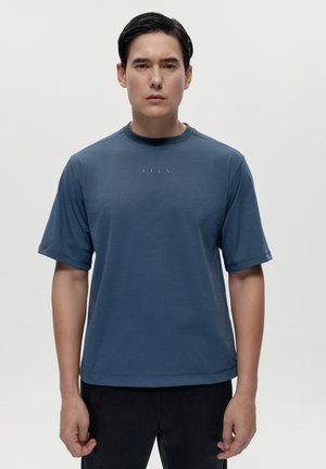 Modré tričko s krátkým rukávem vyrobené z měkké tkaniny, s kulatým výstřihem a minimalistickým logem vyšitým na hrudi. Jednoduchý design a střih.