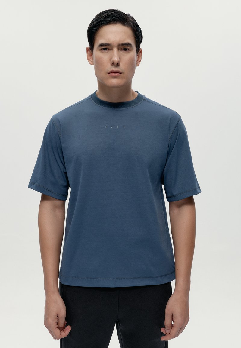 Blå kortärmad t-shirt i mjukt tyg, med rundad halsringning och en minimalistisk logotyp sydd på bröstet. Enkelt design och passform.