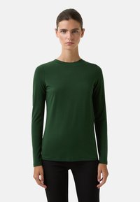 Haut à manches longues, col rond en tissu vert foncé, texture lisse, design ajusté, détails minimalistes, associé à un pantalon noir.