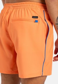 Bañadores de hombre en un brillante color naranja, con un bolsillo con cremallera lateral resaltado con ribetes azules y una cinturilla elástica para mayor confort.
