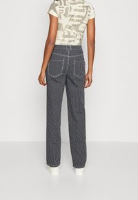 Pantalon à jambes larges rayé en tissu bleu marine et blanc, avec une taille haute, des poches arrière et des détails de couture apparents.