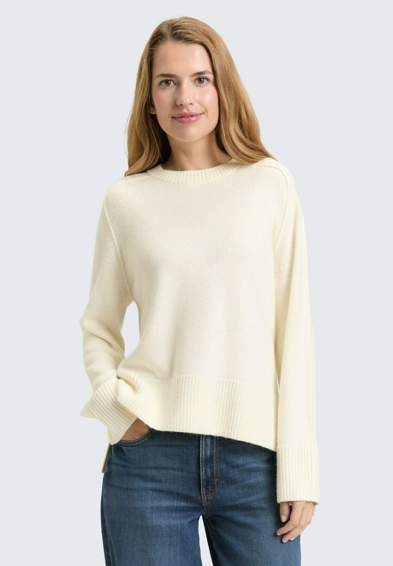 Maglione lavorato a maglia color crema con polsini e orlo a coste, caratterizzato da una vestibilità comoda e scollatura rotonda, abbinato a jeans blu.