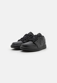 Par med svarte low-top joggesko med lisser, perforert tåområde og en swoosh-logo på siden, vist mot en hvit bakgrunn.