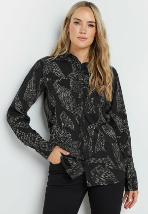 Chemise noire avec un motif abstrait blanc, à boutons, à manches longues et avec un col. Tissu doux avec une texture lisse et une coupe ajustée.