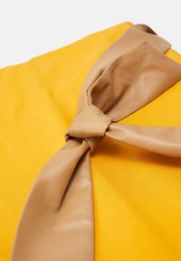 Żółty materiał o gładkiej fakturze z centralnym akcentem z jasnobrązowej skóry w formie węzła, prezentujący minimalistyczny design.