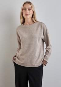 Maglione texturizzato marrone chiaro con scollo rotondo, maniche lunghe con polsini marrone scuro e vestibilità comoda. Indossato con pantaloni neri.
