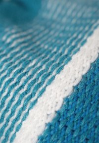 Knit fabric featuring alternating shades of turquoise and white, with a textured pattern and a smooth, soft finish.