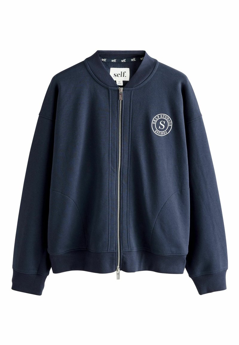 Granatowa kurtka typu bomber na zamek, wykonana z miękkiego materiału, z okrągłym emblematem na piersi, prążkowanym kołnierzem, mankietami i dolnym wykończeniem oraz bocznymi kieszeniami.