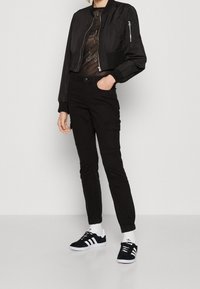 Svart bomberjacka med ribbade manschetter, ihopparad med svarta cargobyxor med sidofickor. Skorna inkluderar svarta sneakers med vita ränder.