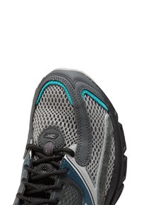 Gros plan sur une chaussure de course en maille grise et teal avec des lacets noirs et une zone de renforcement au niveau des orteils, mettant en avant un tissu respirant et un design durable.