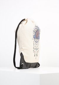 Sac à cordon en toile crème avec un fond en cuir noir, orné d'un motif mandala coloré avec des accents suspendus.