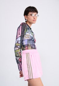 T-shirt à manches longues avec un imprimé de paysage urbain multicolore, associé à un short rose avec des bandes latérales beiges et une taille élastique.
