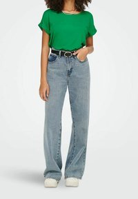 Camicetta verde a maniche corte, jeans in denim blu chiaro a vita alta, cintura nera, sneakers bianche, look casual, tessuto morbido, design a gamba dritta.