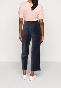 Rosa kortärmad t-shirt, marinblå vida velourbyxor och vita sneakers, sedd bakifrån. Har en logotyp på t-shirten och en slät textur.