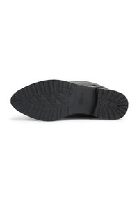 Semelle de botte noire avec un motif de crampons profond et un nom de marque en relief sur le talon, présentée horizontalement sur un fond blanc.