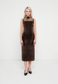 Μίντι φόρεμα από καφέ βελούδο με ψηλό λαιμόκοψη, χωρίς μανίκια και διακριτή υφή. Συνδυασμένο με μαύρες γόβες μυτερές.