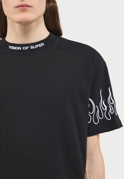 Must musta t-särk, millel on tikitud krae "VISION OF SUPER" ja valged leegigraafikud vasakul varrukal. Silmapaistev tekstuur, mugs rõivastus.