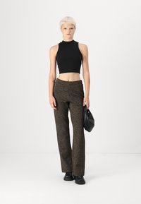 Čierny bezrukávový crop top, hnedé vzorované nohavice s vysokým pásom, čierna taška a robustné čierne topánky na bielom pozadí.