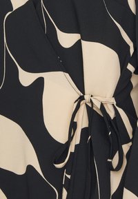 Tessuto a motivi nero e beige con una texture fluida; presenta una chiusura al centro con legature arricciate, creando forme morbide e ondulate.