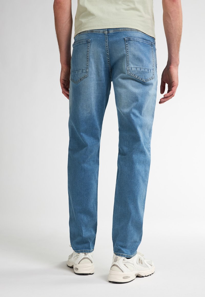 Hellblaue Jeans im geraden Schnitt, mit zwei Gesäßtaschen und einer leicht ausgewaschenen Textur. Kombiniert mit weißen Sportschuhen.