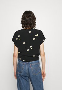 Top nero a maniche corte con ricami di margherite bianche e gialle. Abbinato a jeans in denim blu a vita alta con tasche posteriori.