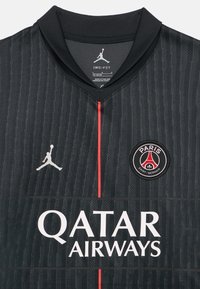 Juoda sportinė apranga su tekstūruotu raštu, kaklelyje raudonas akcentas, baltas „QATAR AIRWAYS“ logotipas ir apvalus klubo herbas.
