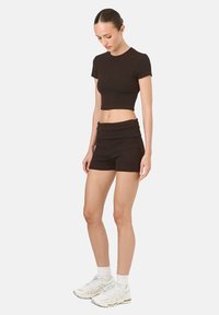 Čierny crop top a šortky s vysokým pásom vyrobené z rebrovaného materiálu. Oblečenie má priliehavý strih a je doplnené bielymi športovými topánkami.